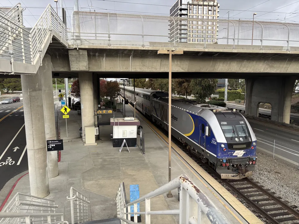 A blue and silver Capitol Corridor train pulling into Santa Clara-Great America station, seen from the pedestrian stairs